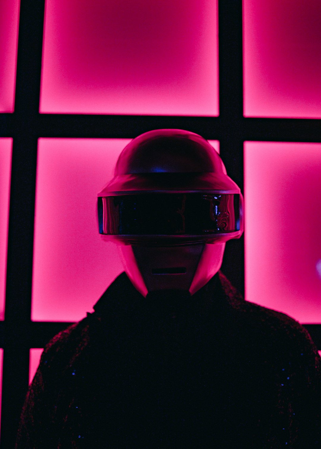 a person wearing a helmet standing in front of a wall of pink squares